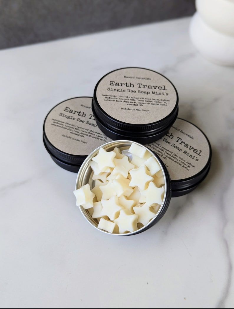 May include: Three round metal tins with black lids. The tins contain star shaped soap bars. The lids have labels that read 'Earth Travel Single Use Soap Mini's'. The labels list the ingredients: Olive Oil, Coconut Oil, Shea Butter, Sodium Hydroxide, Coconut Milk, Castor Oil,  Botanicals and/or herbs. Includes a Mini Soap.