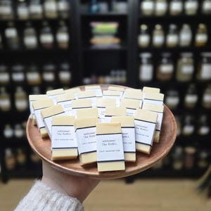 May include: A wooden tray filled with rectangular bars of handmade soap. The soap bars are wrapped in white paper with the text "Welcome! The Roth's" printed on them.