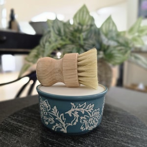 K&ouml;nnte beinhalten: Eine blaue Keramikschale mit wei&szlig;em Blumenmuster, die einen Holzgriff mit Naturborsten h&auml;lt.