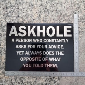 May include: Black sign with white text that reads "ASKHOLE A PERSON WHO CONSTANTLY ASKS FOR YOUR ADVICE. YET ALWAYS DOES THE OPPOSITE OF WHAT YOU TOLD THEM."