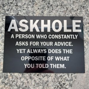 May include: A black sign with white text that reads "ASKHOLE A PERSON WHO CONSTANTLY ASKS FOR YOUR ADVICE. YET ALWAYS DOES THE OPPOSITE OF WHAT YOU TOLD THEM."