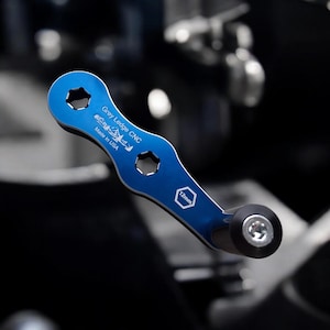May include: A blue CNC tool with a black handle. The tool has two hexagonal openings and the text "Grey Ledge CNC Made in USA" and "12mm" printed on it. The tool is designed for mechanical work.