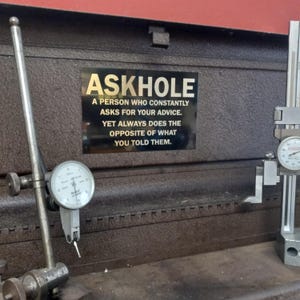 May include: A gold metal sign with black background and white lettering that reads "ASKHOLE A PERSON WHO CONSTANTLY ASKS FOR YOUR ADVICE. YET ALWAYS DOES THE OPPOSITE OF WHAT YOU TOLD THEM."