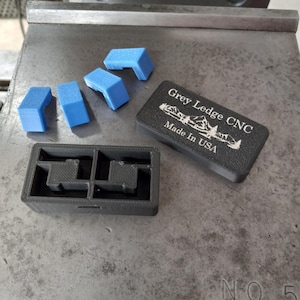 May include: A black plastic box with four compartments, each containing a blue plastic corner piece. The box is labeled "Grey Ledge CNC Made in USA".