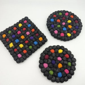以下が含まれることがあります： グレーの背景にカラフルなフェルトボールがついた、丸いフェルトコースターが3つ。コースターは形とサイズが異なります。