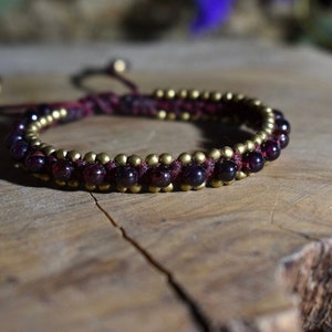 Könnte beinhalten: Ein rotes und goldenes Perlenarmband mit einem geflochtenen Kordelverschluss. Das Armband besteht aus kleinen, runden, dunkelroten Perlen und goldenen Perlen.