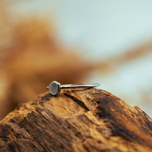 Könnte beinhalten: Ein silberner Ring mit einem sechseckigen Band. Der Ring liegt auf einem Stück verwittertem Holz.