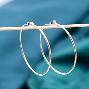 May include: Two silver hoop earrings hanging on a wooden stick against a teal background.