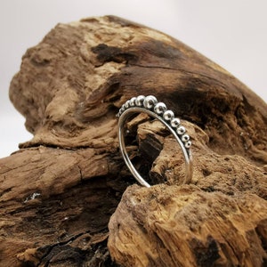 Puede incluir: Un anillo de plata con una fila de pequeñas cuentas redondas alrededor de la banda.