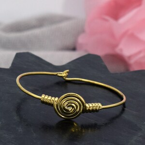 Könnte beinhalten: Ein goldfarbenes Armkettchen mit einem Spiraldesign. Das Armband ist aus dünnem Draht gefertigt und hat einen schlichten, eleganten Look.