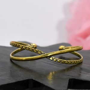 Könnte beinhalten: Ein goldfarbenes, doppeltes Armkettchen mit einem Kreuzmuster. Das Armband ist offen und verstellbar.