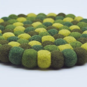 May include: A round green and yellow felt coaster made of small balls of wool.