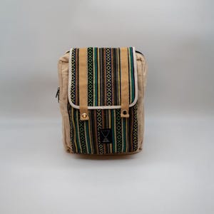 Könnte beinhalten: Eine rechteckige Tasche aus beigem Canvas mit einer Frontklappe, die ein vertikales Streifenmuster in Schwarz, Gelb, Türkis und Weiß aufweist. Die Klappe hat zwei hellbraune Riemen mit Metalldruckknöpfen und ein kleines schwarzes Etikett.