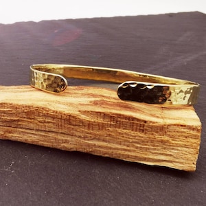 Könnte beinhalten: Ein goldfarbenes, gehämmertes Armreif-Armband. Das Armband ist aus dickem Metall gefertigt und hat eine strukturierte Oberfläche.