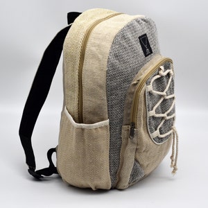 Op de afbeelding: Een beige en zwarte hennep rugzak met een ritsvak en een trekkoord sluiting. De rugzak heeft een geometrisch patroon en een klein driehoekig logo met de tekst "Hemp" erin.
