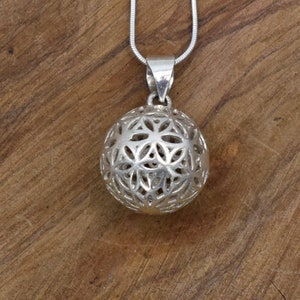 Könnte beinhalten: Eine silberne Halskette mit einem runden Anhänger mit einem komplizierten geometrischen Muster. Der Anhänger ist aus Metall gefertigt und hat ein filigranes, durchbrochenes Muster.