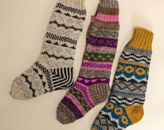 May include: Three colorful knitted socks with patterned designs. One sock is beige with blue and black patterns, another is brown, pink, and purple, and the third is yellow, blue, and gray. The socks are made of a thick, warm material.