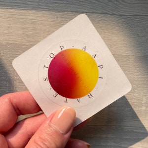 May include: A white square sticker with a red and yellow gradient circle in the center. The circle has the words "H.A.P.I.  T.S.O.P." written around it.