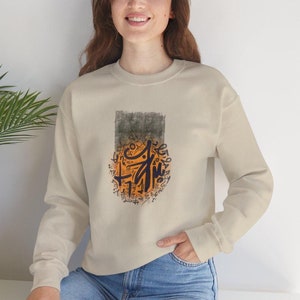 Puede incluir: Una sudadera beige con un estampado gráfico circular que presenta caligrafía naranja y azul sobre un fondo gris.