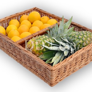 Op de afbeelding: Een rechthoekige rieten mand verdeeld in twee secties. De ene kant is gevuld met felgele sinaasappels, de andere met een groene ananas. De mand is gemaakt van geweven bruin riet en staat op een witte ondergrond.