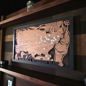 May include: Wooden baseball stadium map art with a black frame. The map is of the United States, with baseballs marking stadium locations. The words "BASEBALL STADIUM MAP" are at the bottom. The map is displayed on a wooden shelf.