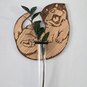 May include: Wooden wall decor featuring a carved otter holding a glass test tube vase with a green plant stem.