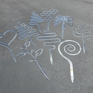 May include: A set of ten metal cookie cutters in various shapes, including a heart, a swirl, a honeycomb, a tree, a leaf, and a ribcage. The cutters are silver and have a shiny finish.