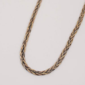 May include: A silver and gold chain necklace with a braided design.