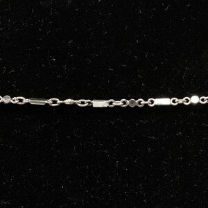 May include: Delicate silver necklace with a chain featuring alternating rectangular and circular links. The necklace is displayed against a black background, highlighting its minimalist design. A fine piece of jewelry.