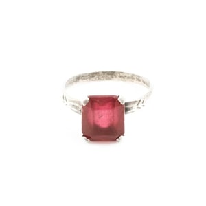 May include: A silver ring with a large, rectangular, deep red gemstone. The band has a textured design, and the gemstone is held by four prongs. The ring is set against a white background.