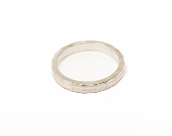 Op de afbeelding: Een zilveren ring met een getextureerde, gehamerde afwerking. De ring is cirkelvormig en ligt op een witte achtergrond. De band heeft een licht onregelmatig oppervlak, waardoor hij een ambachtelijke uitstraling heeft. Deze ring is een sieraad.
