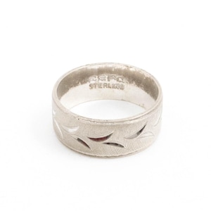 May include: A silver ring with a leaf pattern. The ring is marked "ESPO STERLING" on the inside. The ring has a textured surface and a series of leaf-shaped cutouts around the band.