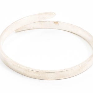 May include: A silver bangle bracelet with a simple, smooth design. The bracelet is open and flexible, making it easy to put on and take off.