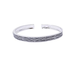 May include: A silver cuff bracelet featuring a detailed woven or braided texture along the outer surface. The bracelet has an open design with smooth, polished edges and a metallic finish, showcasing a consistent pattern throughout the band.