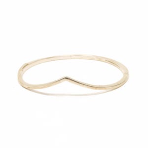 May include: A gold-coloured bracelet with a V-shaped design. The bracelet is circular with a V-shaped dip in the centre. The bracelet is made of a shiny, metallic material. The bracelet is shown on a white background.