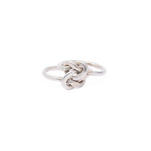 May include: A silver-toned ring featuring a central knot design. The band is smooth and circular, connecting to a decorative, intertwined knot element at the front. The metal has a polished, reflective finish throughout the entire structure.