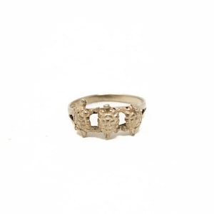 Peut inclure: Une bague argentée avec un motif texturé et détaillé. La bague présente une série de formes ornementales reliées autour de l'anneau, créant un aspect unique et accrocheur. La bague est posée sur un fond blanc uni.