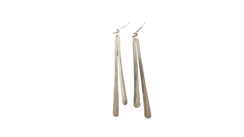 Pu&ograve; includere: Un paio di orecchini pendenti color argento. Ogni orecchino presenta un lungo design sottile a forma di goccia. Gli orecchini pendono da un semplice gancio. Lo sfondo &egrave; bianco.
