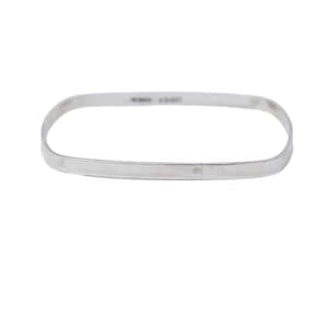 Peut inclure: Un bracelet jonc de couleur argentée avec une forme rectangulaire et des coins arrondis. La bande métallique présente une finition lisse et polie avec une largeur uniforme sur toute sa circonférence, incluant de petits poinçons gravés.