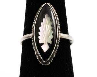 May include: A silver ring with an oval black onyx stone. The stone features a carved white leaf design. The ring has a detailed silver border and is displayed on a black surface.