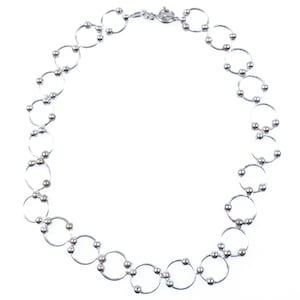 May include: A silver-toned necklace composed of a series of interconnected circular links. Each circular link is accented with small, spherical beads positioned at the points where the rings join together. The necklace features a circular clasp closure.