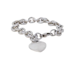 Könnte beinhalten: Ein silberfarbenes Gliederarmband mit einem einzelnen herzförmigen Anhänger. Das Armband besteht aus kreisförmigen Metallgliedern und verfügt über einen kleinen Karabinerverschluss. Der herzförmige Anhänger ist glatt und poliert.