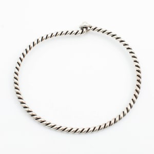 May include: A silver-colored, twisted rope-style bracelet. The bracelet is circular with a small, rounded knot at the top. The design features a series of tightly wound, parallel lines, creating a textured appearance. The background is plain white.