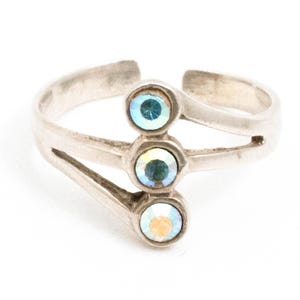 May include: A silver-toned ring featuring three iridescent, round gemstones. The ring has a split band design with the gemstones set in a vertical line. The gemstones reflect a range of colors, including blue, green, and yellow.