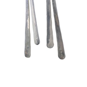 Pu&ograve; includere: Primo piano di quattro utensili in metallo argentato con manici strutturati. Gli utensili sono disposti su uno sfondo bianco. Ogni utensile ha una forma leggermente diversa e un piccolo segno vicino alla base del manico.