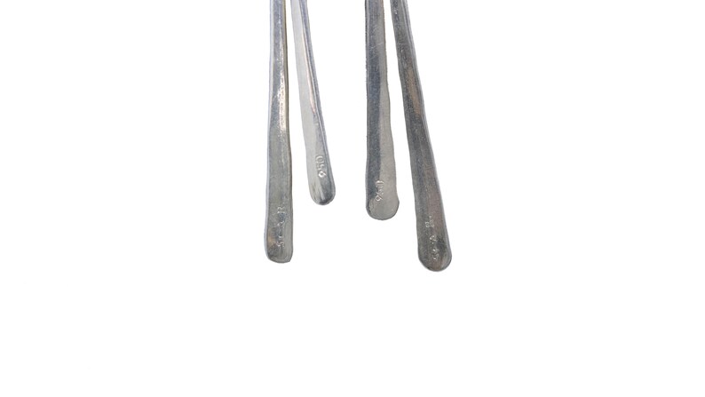 Pu&ograve; includere: Primo piano di quattro utensili in metallo argentato con manici strutturati. Gli utensili sono disposti su uno sfondo bianco. Ogni utensile ha una forma leggermente diversa e un piccolo segno vicino alla base del manico.