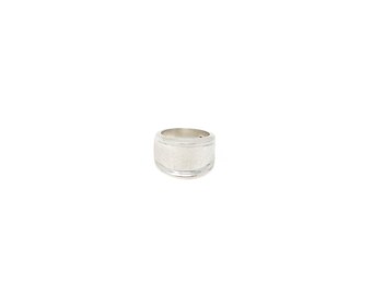 May include: A wide silver band ring with a smooth, polished finish. The ring features a slightly concave center section bordered by two raised, thin horizontal lines along the top and bottom edges, creating a clean and simple metallic design.