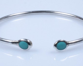 May include: A silver open cuff bracelet with a turquoise stone at each end. The bracelet has a simple, minimalist design. The turquoise stones provide a splash of colour. The bracelet is suitable for everyday wear.