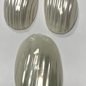 Peut inclure: Trois cabochons ovales en nacre blanche avec un motif strié.