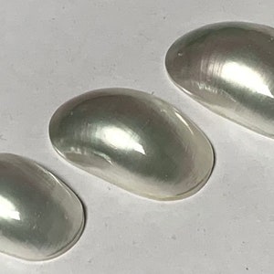 Op de afbeelding: Drie iriserende, witte, ovale parelmoer cabochons in verschillende maten.